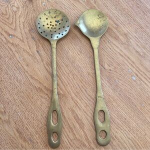 Two antique brass kitchen utensils, a strainer and a serving spoon.